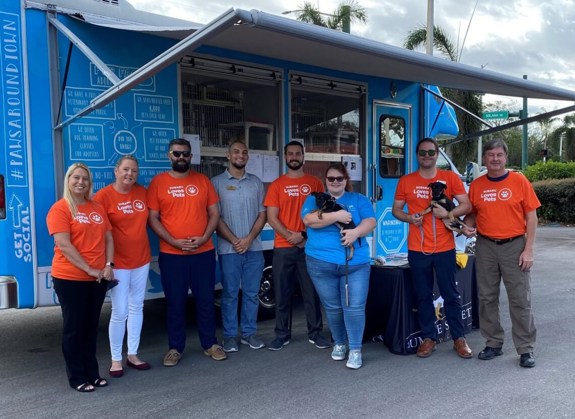 Subaru of Naples team members standing in front of a pet adoption truck holding puppies.