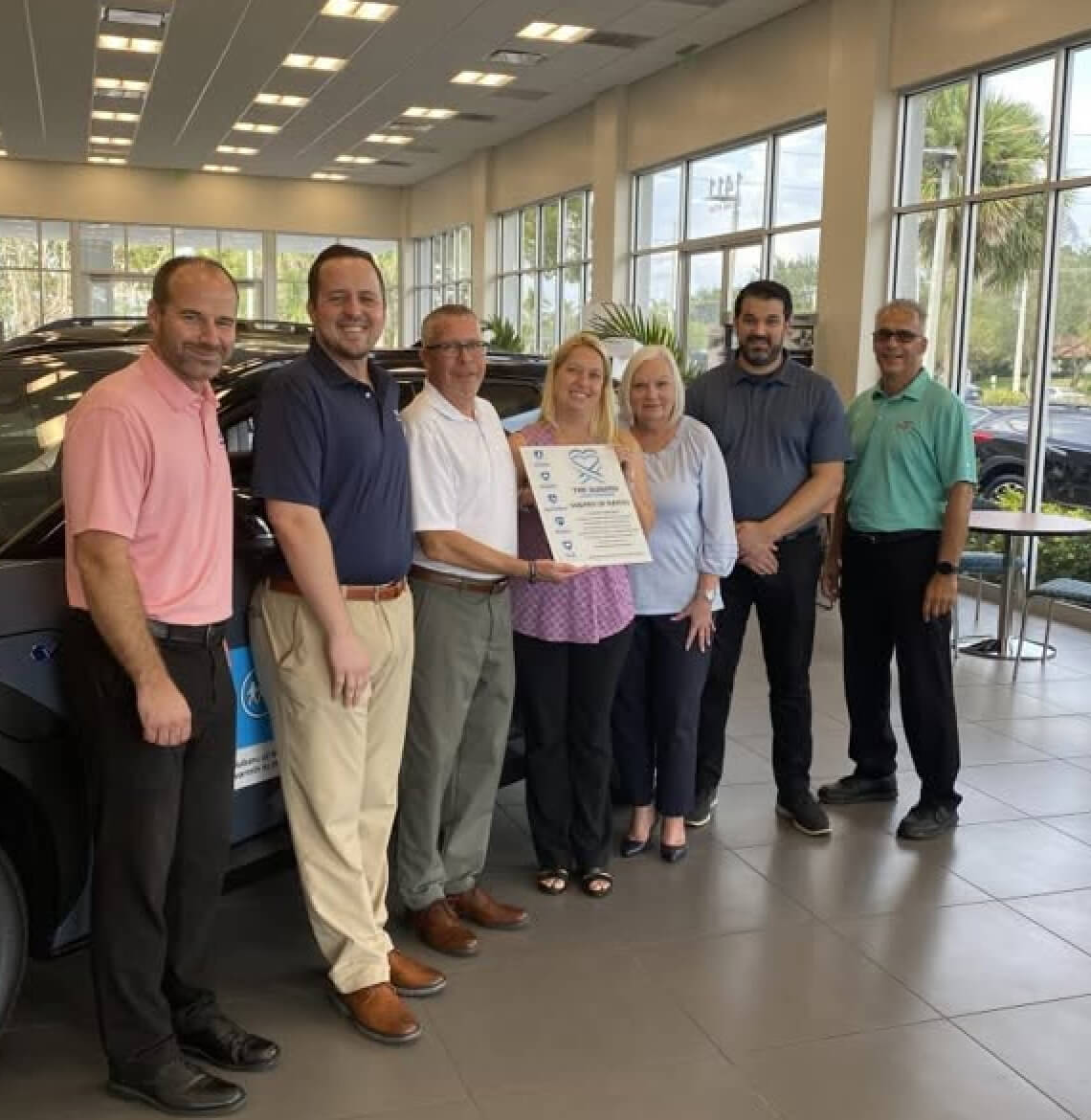 Subaru of Naples team standing in a row accepting an award inside a bright, clean dealership.