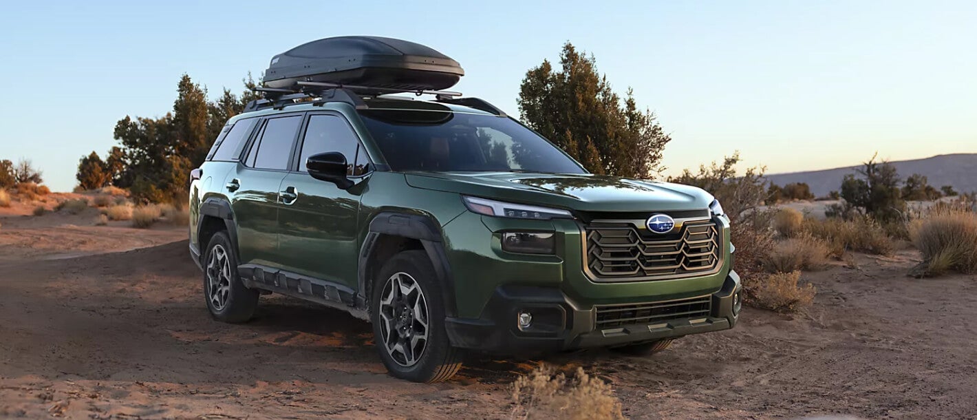 A green Subaru Outback parked in a desert clearing.