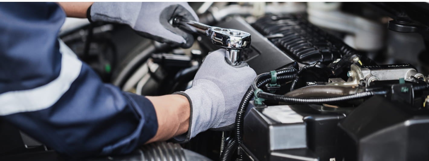 Service technician using a ratchet while working on a vehicle engine.