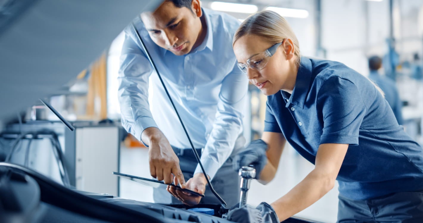Technician servicing a vehicle while another person reviews the work on a tablet.