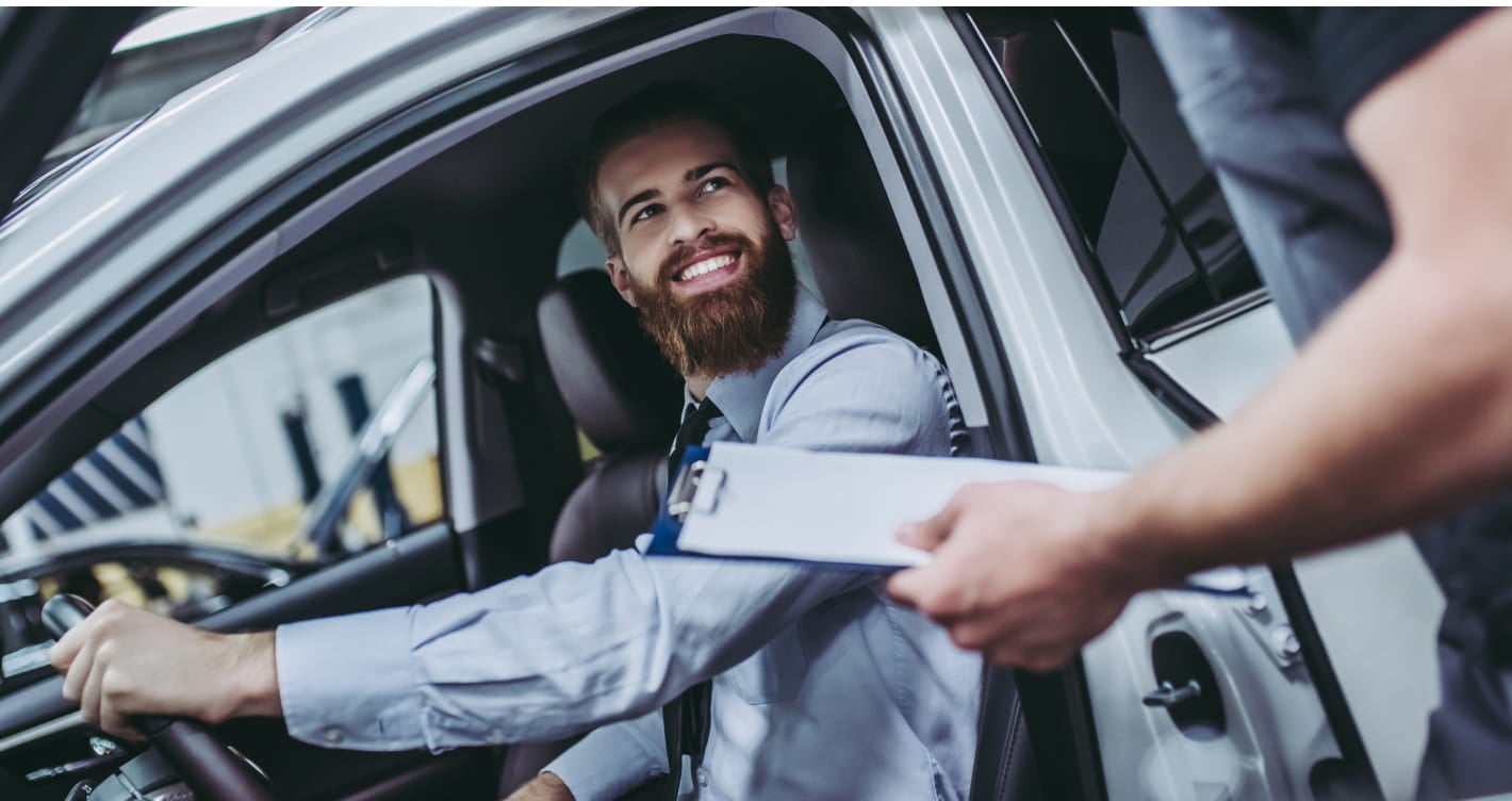 Customer seated in a vehicle speaking with a service advisor holding a clipboard.