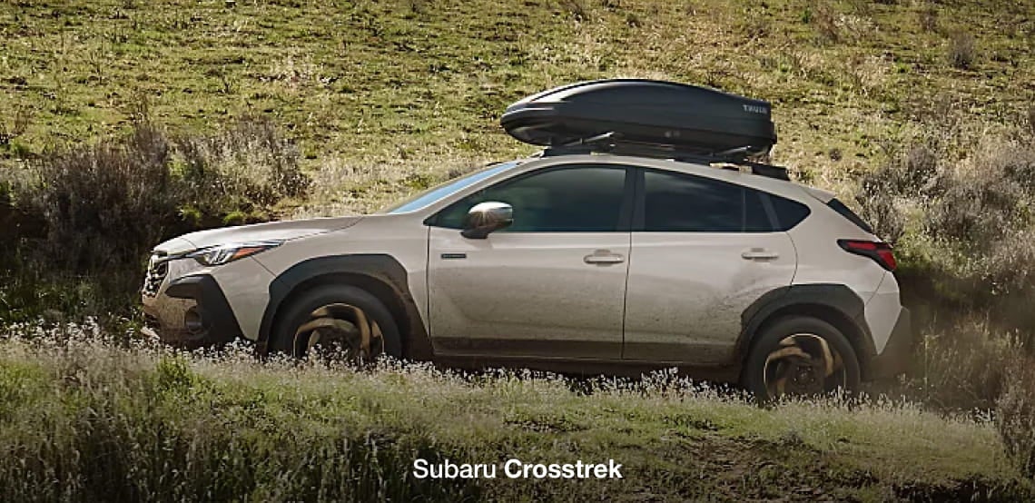 Subaru Crosstrek driving off-road through a grassy landscape with a rooftop cargo box.