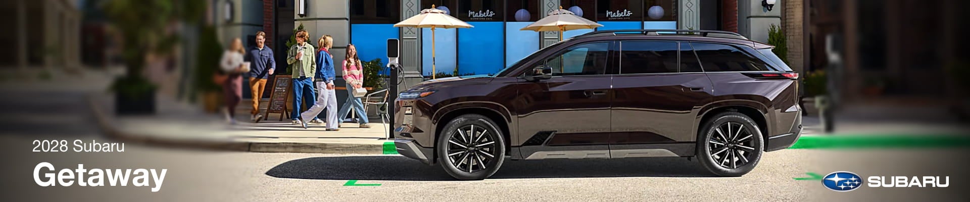 2028 Subaru Getaway electric SUV parked at a curbside charging station in an urban shopping area.