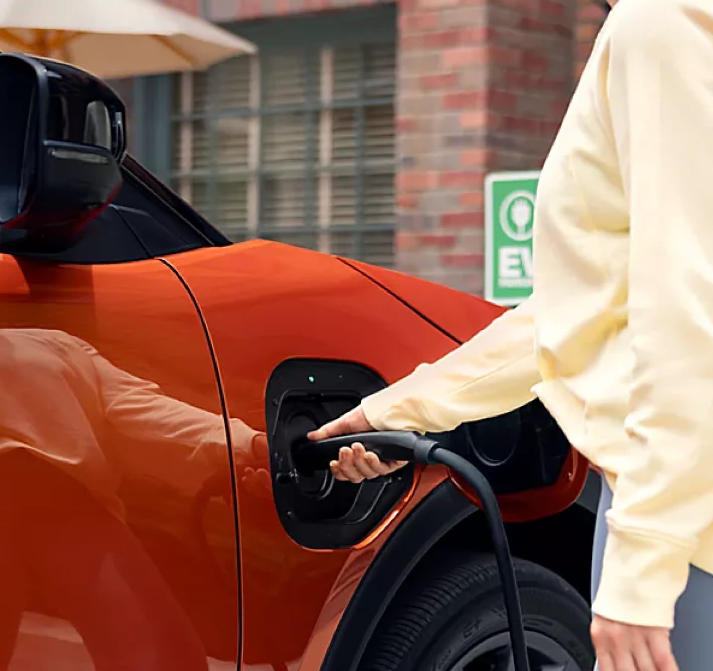  Person connecting a charging cable to the charging port of an orange electric SUV.
