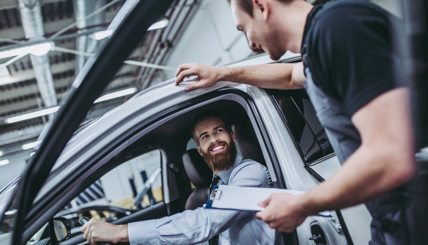 Customer seated in the driver's seat while speaking with a dealership representative holding a clipboard beside the vehicle.