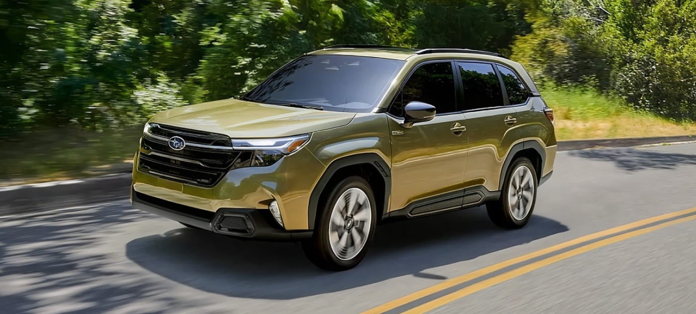 Green Subaru Forester SUV driving along a tree-lined road, shown from a front three-quarter angle with lush greenery in the background.