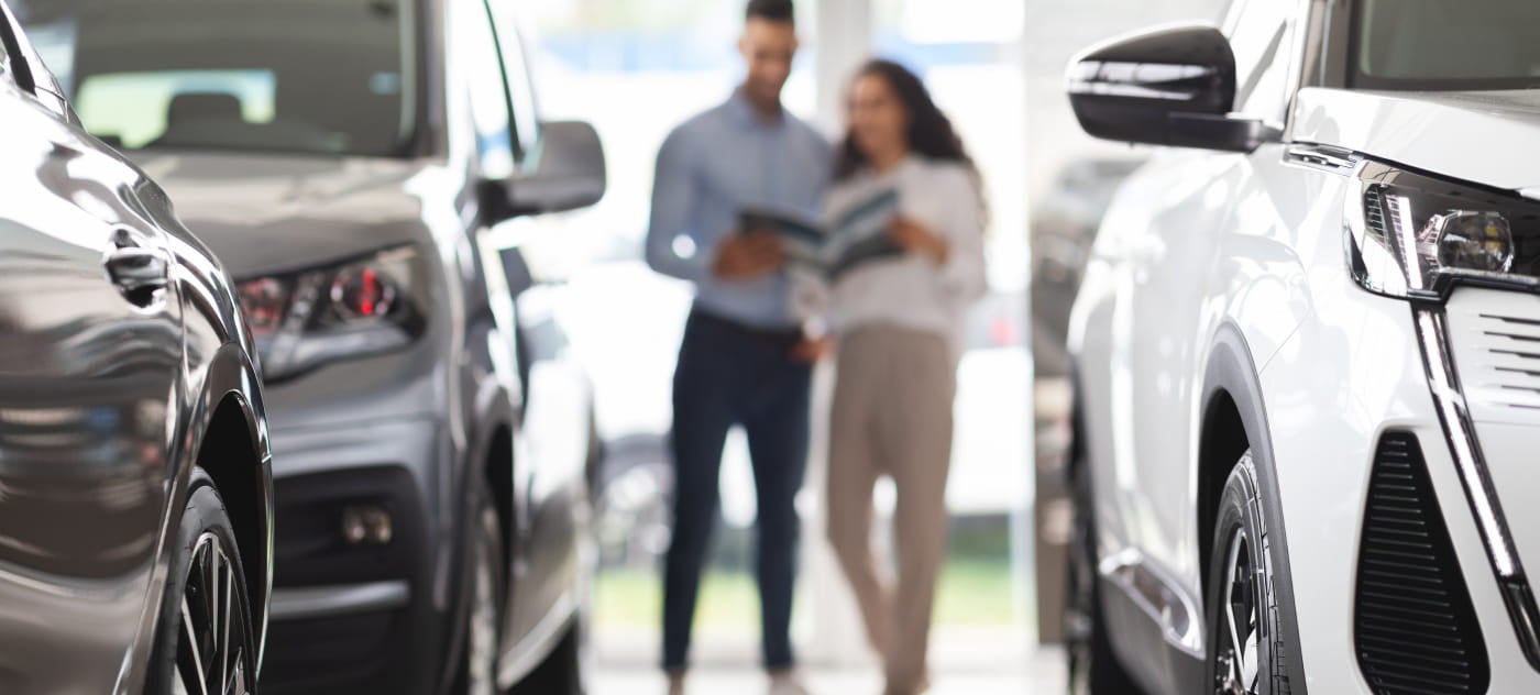 Two customers reviewing a brochure while browsing vehicles inside a car dealership showroom.
